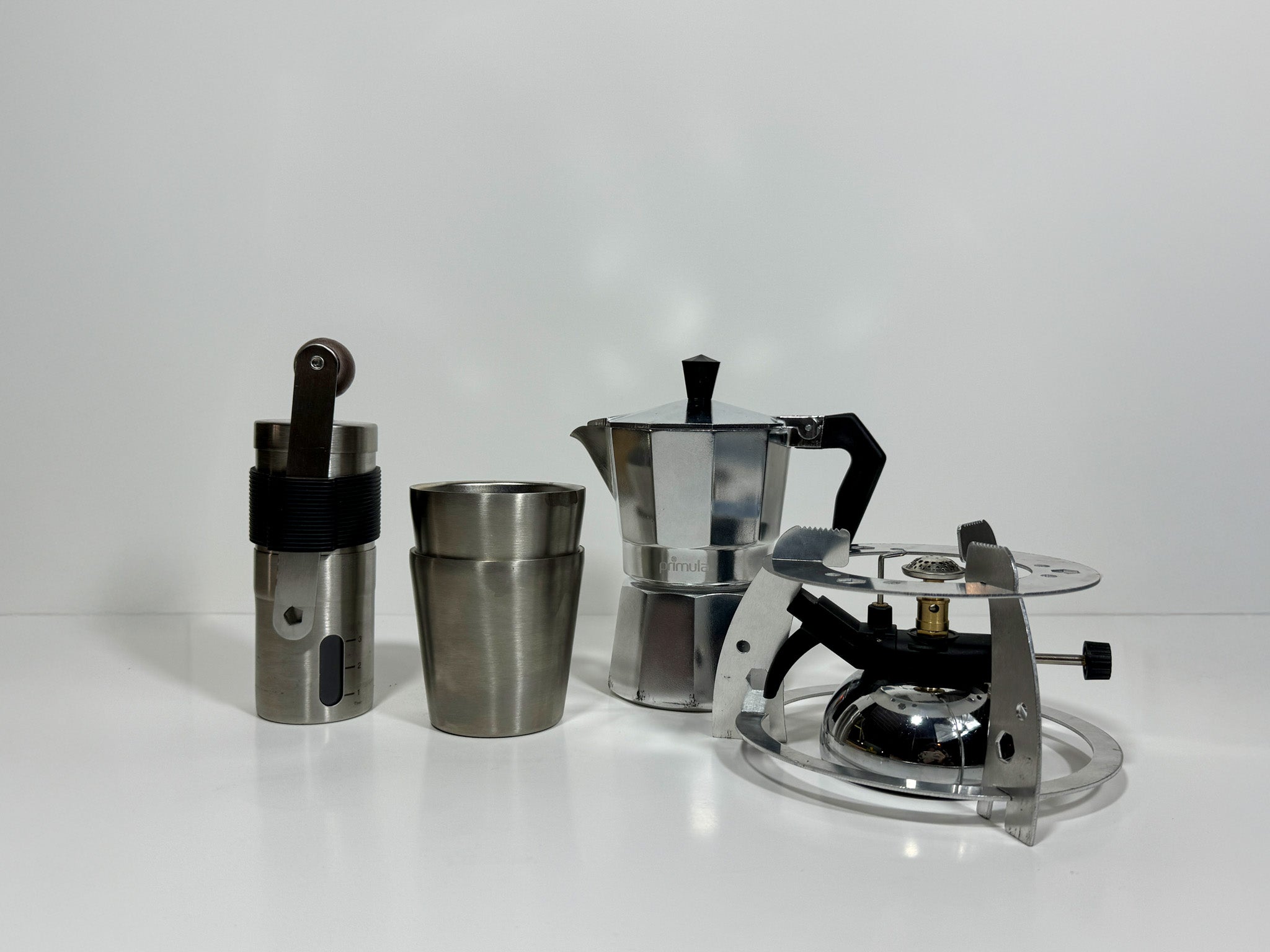 2 insulated stainless steel mugs, a portable espresso and coffee maker, a hand-crank coffee grinder, and a mini tabletop butane burner