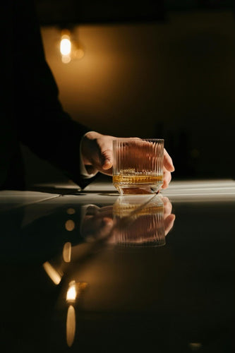 person holding clear whiskey glass